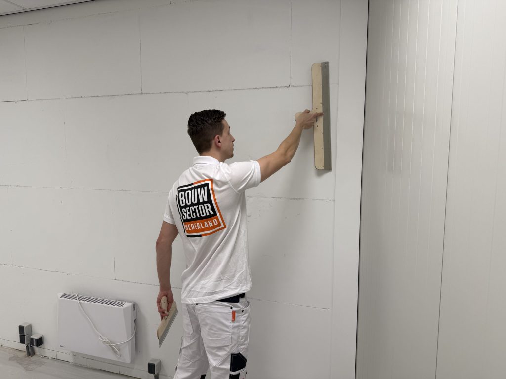 Stukadoor van Bouwsector Nederland strijkt een wand glad met een spaan naast een radiator