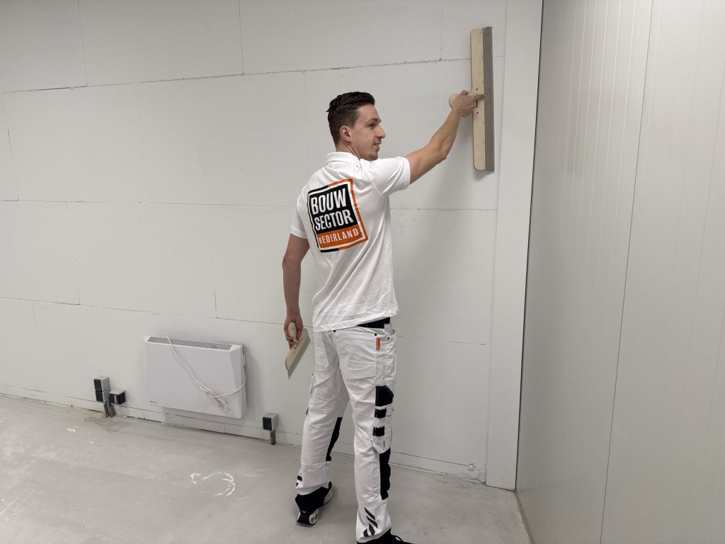 Stukadoor van Bouwsector Nederland trekt een stuclaag glad op een wand met een radiator eronder