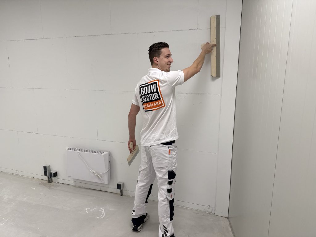 Stukadoor van Bouwsector Nederland strijkt met een spaan een witte wand glad