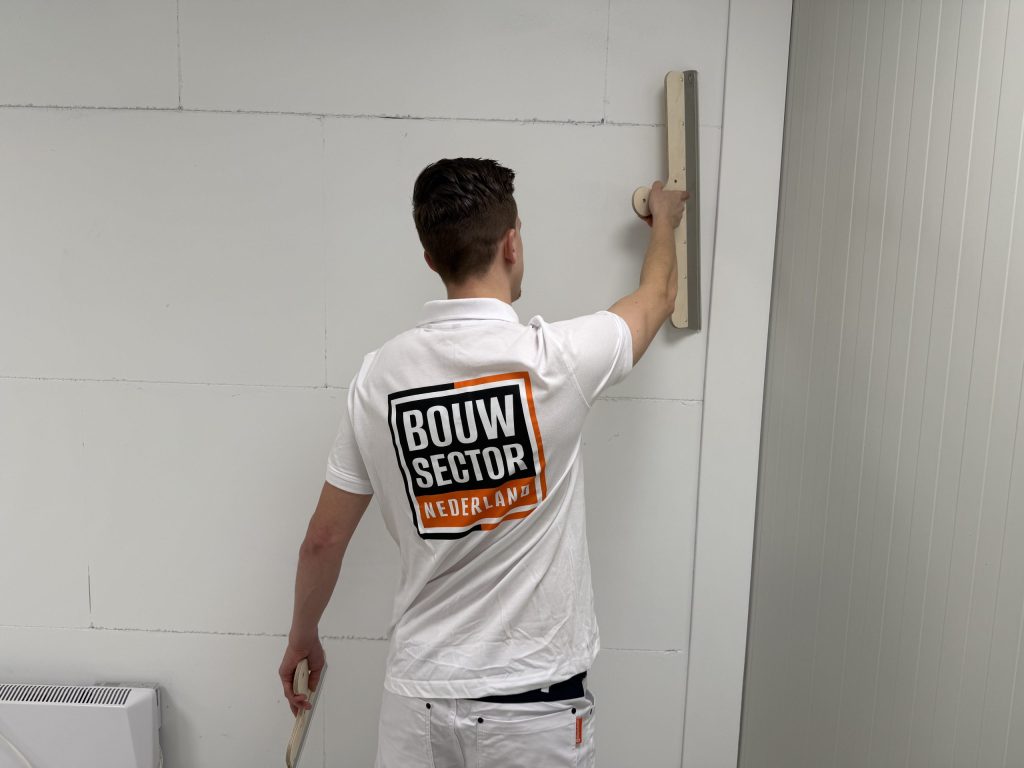 Stukadoor van Bouwsector Nederland strijkt met een spaan de bovenkant van een wand glad