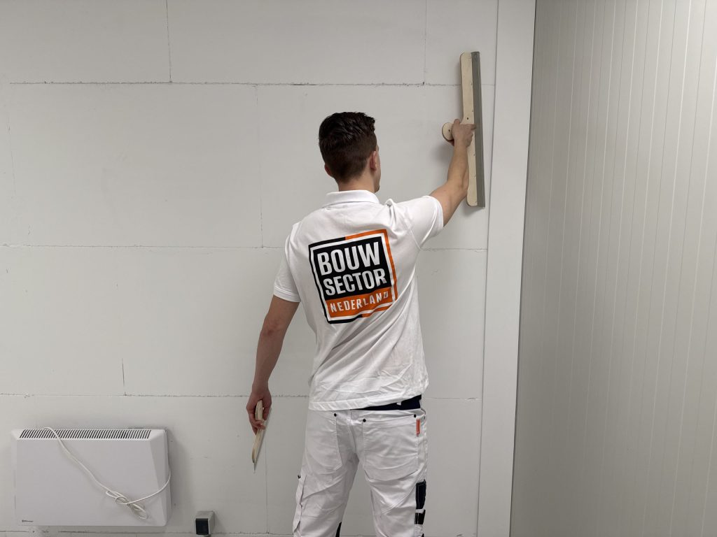 Stukadoor van Bouwsector Nederland met een spaan bij een witte wand naast een radiator