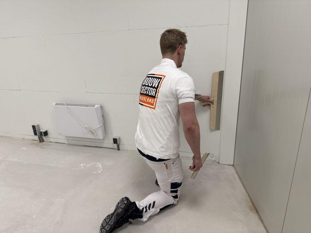 Stukadoor van Bouwsector Nederland zit op zijn knie en werkt het onderste deel van een wand af