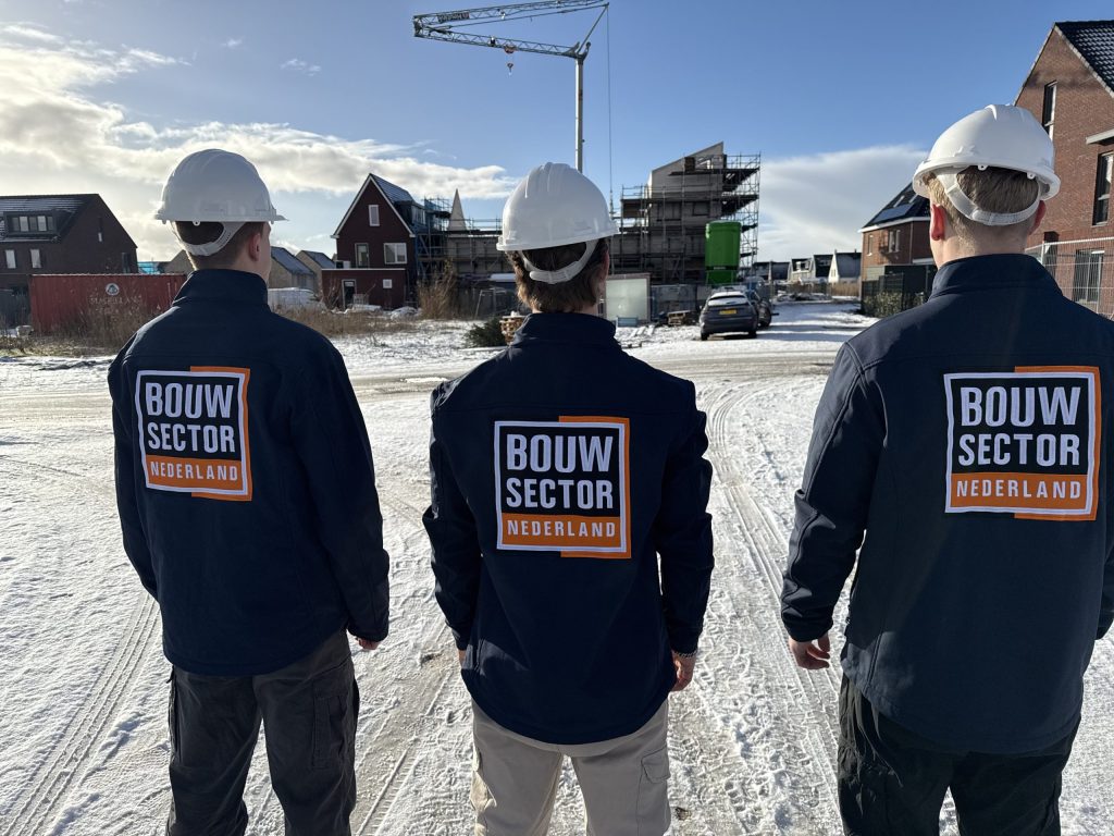 Drie vakmensen van Bouwsector Nederland met witte helm bij een nieuwbouwwijk met een bouwkraan