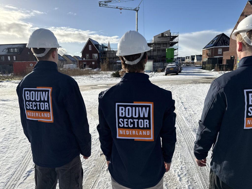 Drie vakmensen van Bouwsector Nederland met witte helm kijken uit over woningen in aanbouw